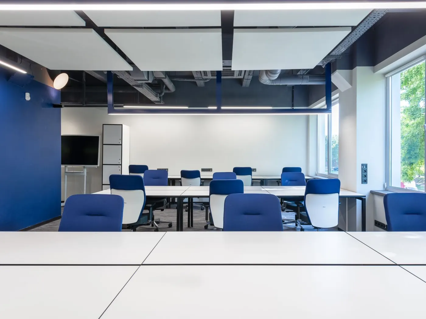 Sala de reuniones con mesas blancas y sillas azules junto a un ventanal